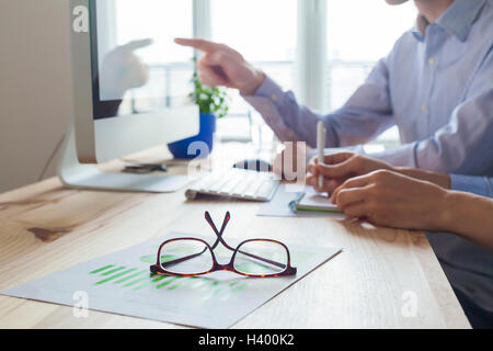 Riunione della gente di affari in co-Ufficio di lavoro, una persona insegnamento l'altra, close-up sui bicchieri Foto Stock
