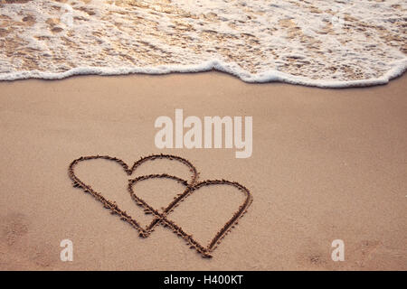 Cuori attirato nella sabbia con seafoam e wave Foto Stock