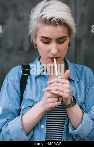Giovani moda donna il fumo di sigaretta in piedi mentre all'aperto Foto Stock