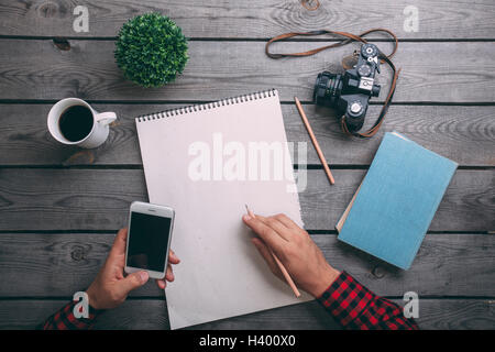 Immagine ritagliata dell uomo con smart phone durante la scrittura su carta a tavola Foto Stock