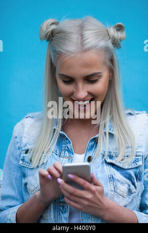Felice di moda giovane donna utilizzando il telefono cellulare contro la parete blu Foto Stock