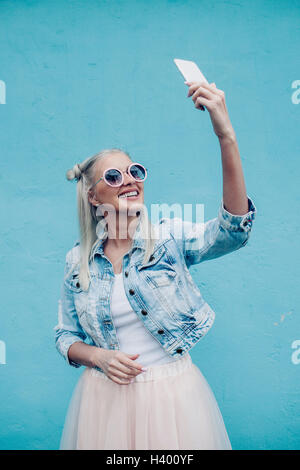 Felice di moda giovane donna parlando selfie contro la parete blu Foto Stock