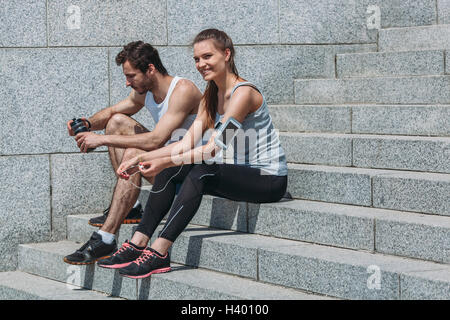 Happy amici in sportswear seduti sui passi dalla parete Foto Stock