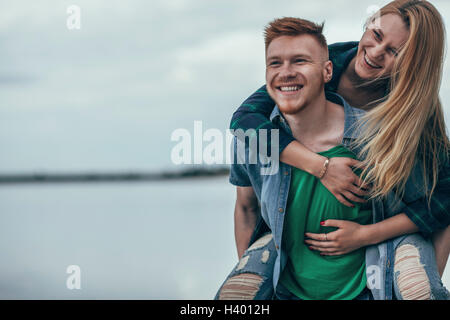 Uomo felice piggybacking allegro ragazza sul lungolago contro sky Foto Stock