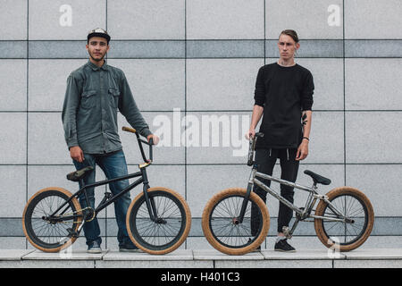 Certi amici in piedi con le biciclette sul marciapiede contro la parete Foto Stock