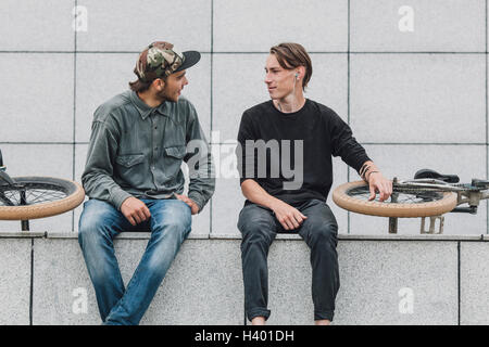 Gli amici di parlare mentre è seduto con le biciclette contro il muro a skate park Foto Stock