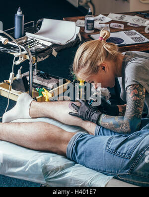 Artista il tatuaggio sul design dell'uomo in gamba studio Foto Stock