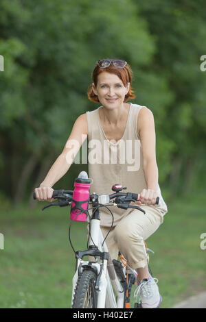 Ritratto di donna sorridente Bicicletta Equitazione in campo al park Foto Stock