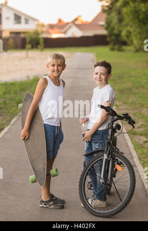 Amici sorridente con lo skateboard e la bicicletta in piedi in posizione di parcheggio Foto Stock