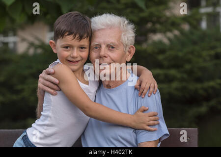 Ritratto del nonno sorridente e nipote abbracciando mentre è seduto in una panchina nel parco Foto Stock