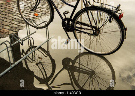 Bicicletta parcheggiata su portabiciclette riflesso in una pozza d'acqua Foto Stock