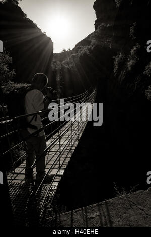 Ponte sospeso su una profonda e dark canyon contro il sole Foto Stock