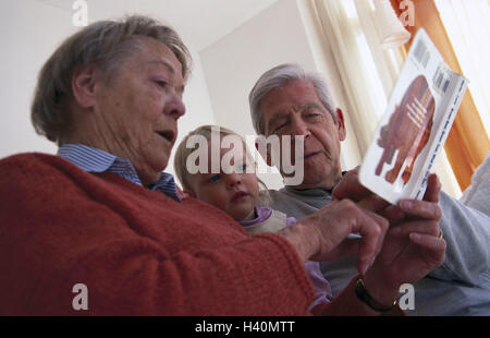 Divano, nonni, nipote, libro, guardare, cittadini anziani, a coppia Senior, 70-80 anni, bambino, infantile, ragazza, 2 anni, nipote, nipote, due generazioni, tempo libero, armonia, attività per il tempo libero, insieme, libro per bambini, leggere, a pictur Foto Stock