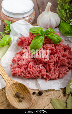 Le carni bovine macinate a crudo su tavola di legno con erbe e spezie Foto Stock
