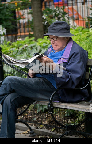 Un vecchio uomo la lettura del New York Times su un banco di lavoro a Washington Square Park nel Greenwich Village di New York City. Foto Stock