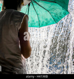 La donna caucasica holding ombrellone vicino a spruzzi d'acqua Foto Stock