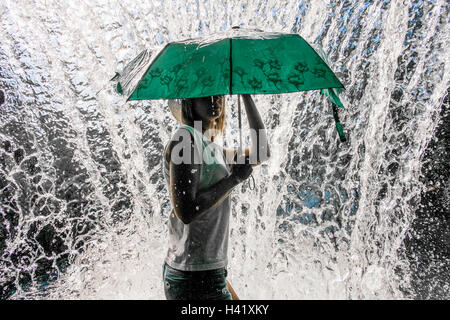 La donna caucasica holding ombrellone vicino a spruzzi d'acqua Foto Stock