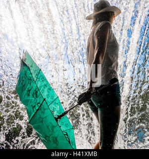 La donna caucasica holding ombrellone vicino a spruzzi d'acqua Foto Stock