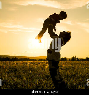 Mari uomo figlio di sollevamento nel campo al tramonto Foto Stock