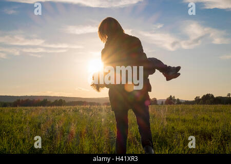 La donna che porta il figlio in campo al tramonto Foto Stock