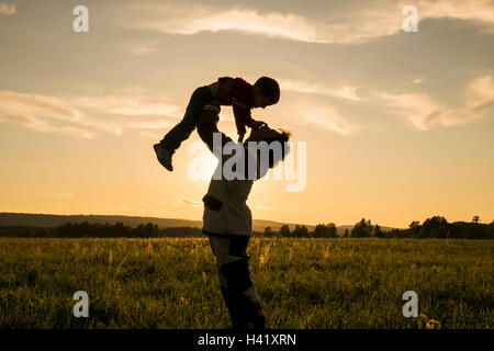 Mari uomo figlio di sollevamento nel campo al tramonto Foto Stock