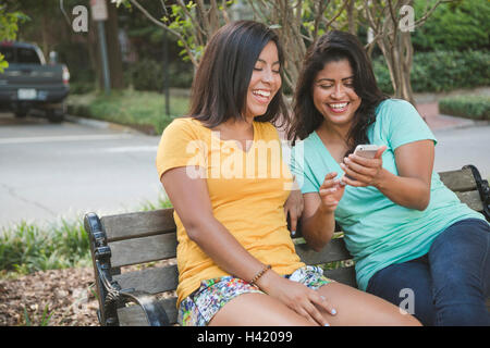 Ispanico madre e figlia tramite telefono cellulare su una panchina nel parco Foto Stock