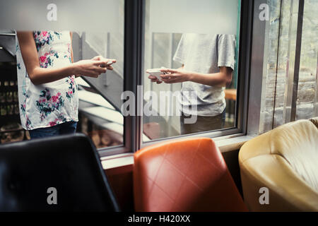 Razza mista fratello e sorella di scrivere messaggi su telefoni cellulari dietro la finestra Foto Stock