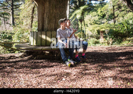 Razza mista del fratello e sorella seduta sul banco a tree Foto Stock