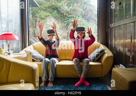 Razza mista del fratello e sorella utilizzando la realtà virtuale gli occhiali sul divano Foto Stock