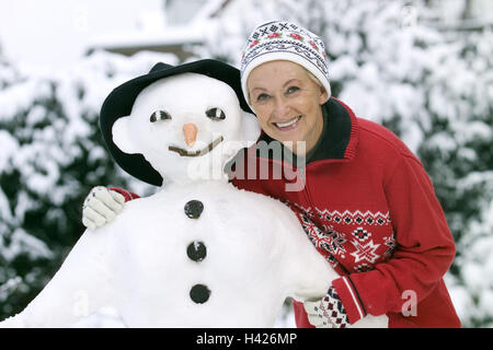 Senior, felice, snowman, ritratto, donna Età migliore, tempo libero, intraprendenti, il divertimento e la gioia della vita, natura spensierata, felice, vestiti, invernale, abbigliamento invernale, guanti, cappuccio, copricapo, stagione invernale, neve, legno, Foto Stock
