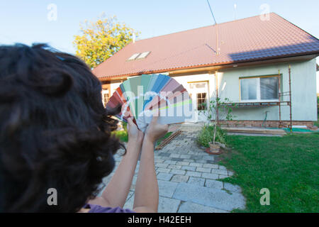 Giovane donna sceglie un nuovo colore per la loro casa. Scegliere i colori per una nuova facciata. (Focus sul campionatore, tutti in primo piano un Foto Stock