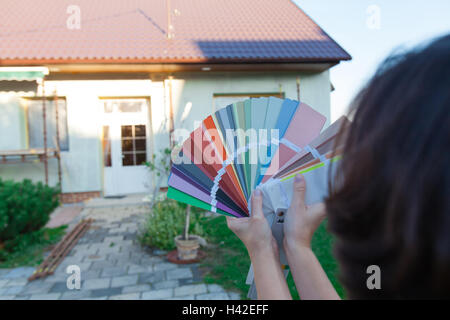 Giovane donna sceglie un nuovo colore per la loro casa. Scegliere i colori per una nuova facciata. (Focus sul campionatore, tutti in primo piano un Foto Stock