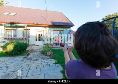 Giovane donna sceglie un nuovo colore per la loro casa. Scegliere i colori per una nuova facciata. (Focus sul campionatore, tutti in primo piano un Foto Stock