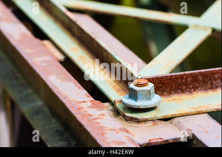 Dettaglio del metallo esagonale fissaggio a vite su un angolo di parzialmente arrugginito barre di acciaio e piastre. Foto Stock