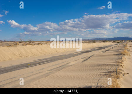 Sabbia soffia attraverso strada vuota nel deserto di Mojave. Foto Stock