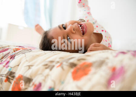 Sorridente razza mista ragazza il rotolamento sul letto Foto Stock