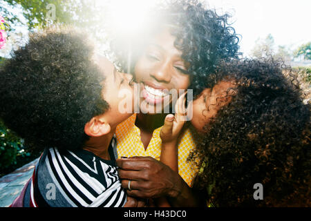 Figlio e figlia baciare le guance di madre all'aperto Foto Stock