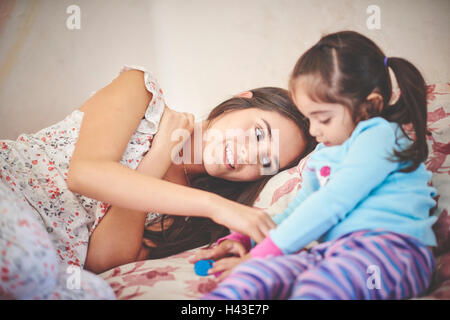 Madre ispanica giocando con la figlia sul letto Foto Stock