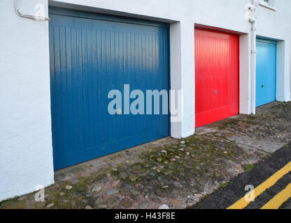 Una fila di rosso, blu e azzurro porte di garage corrono in parallelo con il doppio di linee gialle dipinte sul bordo delle strade. Foto Stock