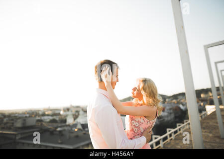 Pretty sunny outdoor Ritratto di giovane coppia elegante mentre baciare sul tetto con vista città Foto Stock