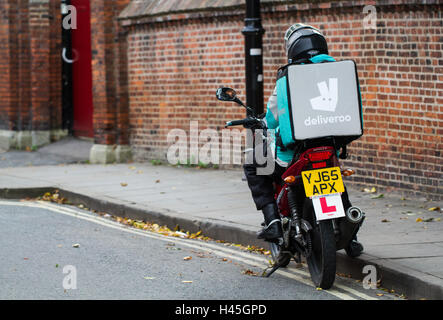 Un motociclista deliveroo dal sempre più popolare il cibo caldo e fast food società di consegna parcheggiato per un ordine. Foto Stock