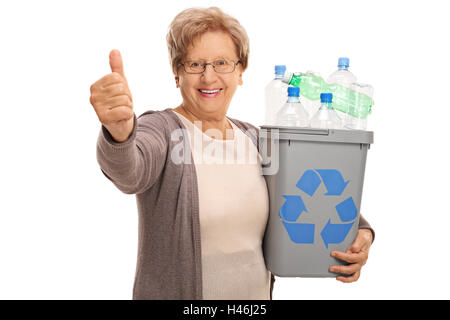 Gioiosa donna anziana tenendo un cestino pieno di bottiglie di plastica e dare un pollice in alto isolato su sfondo bianco Foto Stock