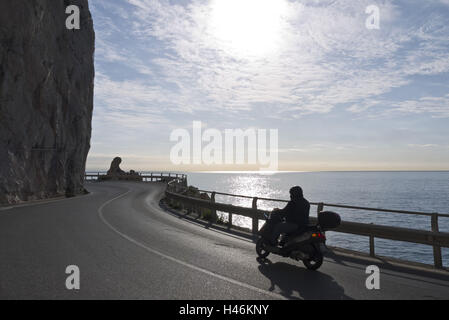 In Italia, la Liguria, Finale Ligure, il Mar Mediterraneo, Küstenstrasse, scooter, scooter, luce posteriore, luce solare, strada costiera, street, avvolgimento, sul mare Foto Stock