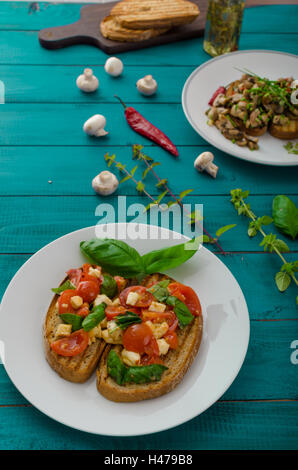 La bruschetta 2 tipi - classic con pomodoro, basilico e mozzarella, secondo tipo con funghi, il peperoncino e le erbe aromatiche Foto Stock