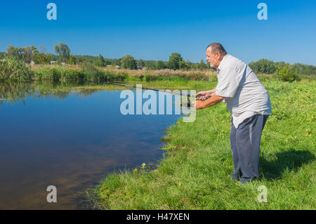 Eccitato pescatore senior in piedi su un fiume con asta di filatura e pronto per la cattura di pesci di fiume piccolo Merla, Ucraina centrale Foto Stock