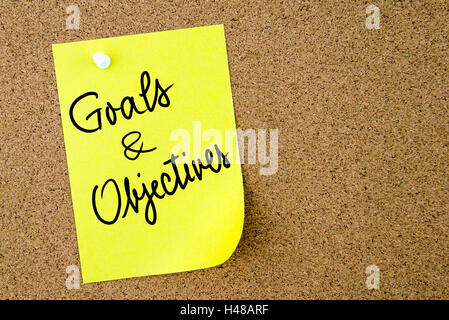 Gli obiettivi e gli obiettivi testo scritto su carta gialla nota appuntata sulla bacheca di sughero con la puntina bianca. Business Concetto di immagine Foto Stock