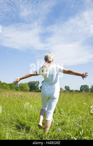 Una donna di mezza età felicemente danze al di sopra di un prato, Foto Stock