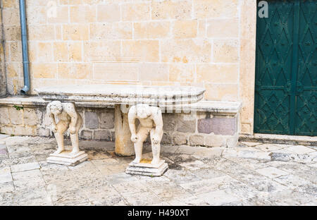 Il tavolo di pietra è supportato da due statue di curvò uomini, in piedi accanto al lato ingresso a Nostra Signora delle rocce, Perast Foto Stock