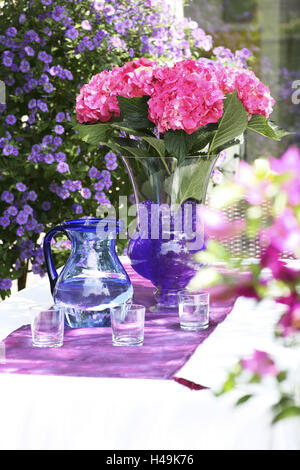 Le Ortensie in vaso sul tavolo da giardino con acqua brocca brocca, bicchieri di vetro, Foto Stock