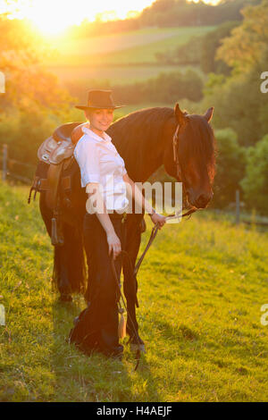 Giovane donna, pony Connemara, stallone, cinghia, vista laterale in piedi, guardando la telecamera, Foto Stock